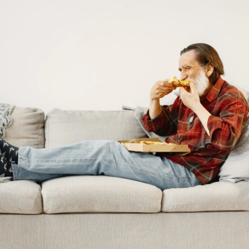 old person eating a pizza while sitting on a sofa