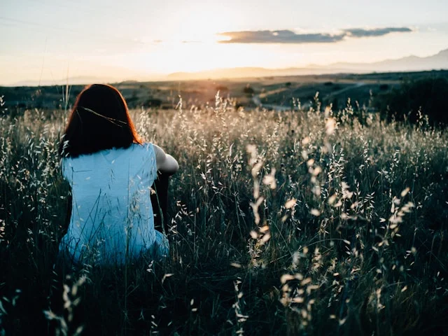 woman sitting on grass field watching sunset